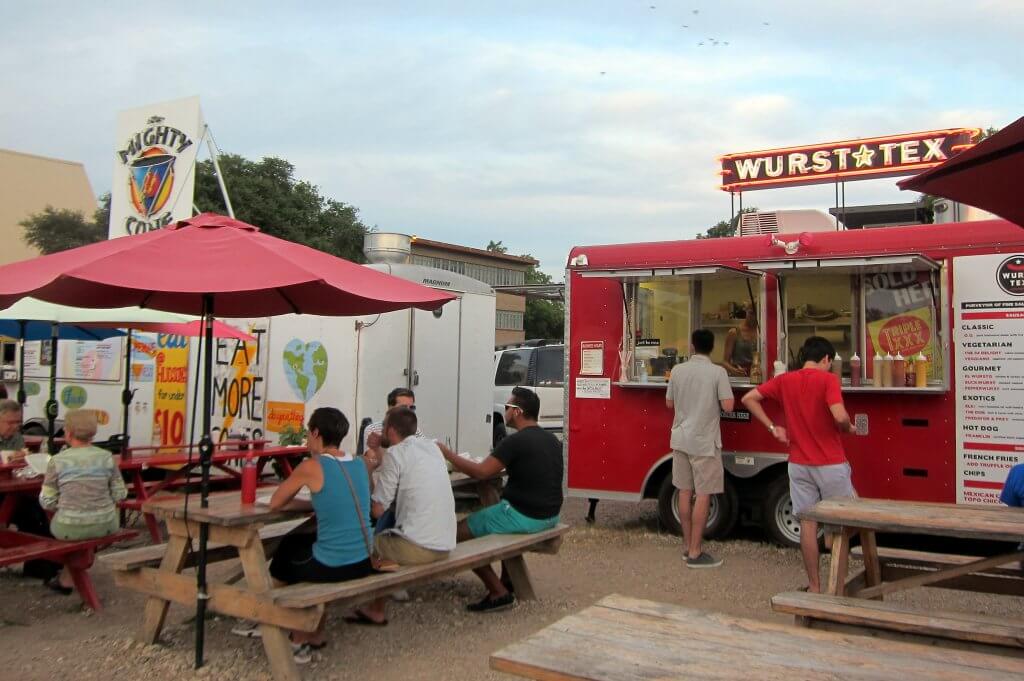 people eating at a picnic table and ordering from food trucks