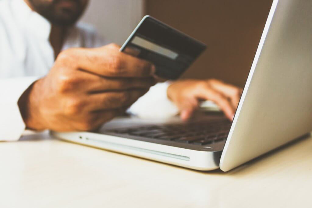 man's hand holding a credit card in front of a laptop computer