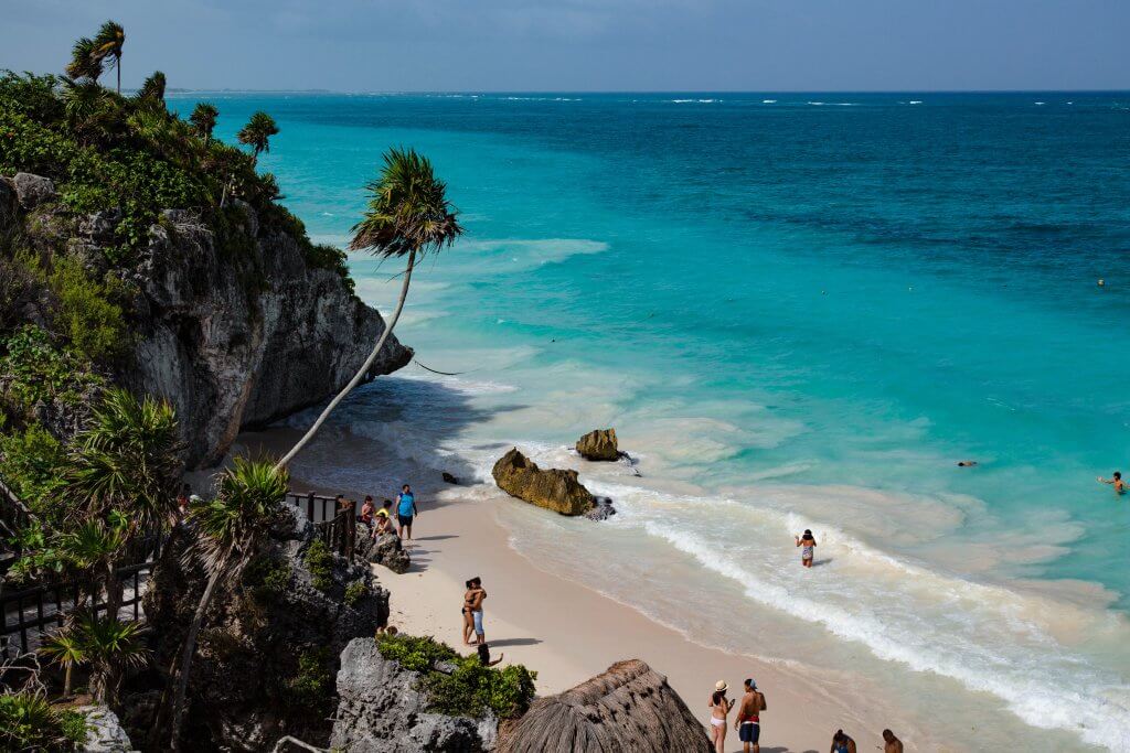 People walk along a cliffside beach in Tulum